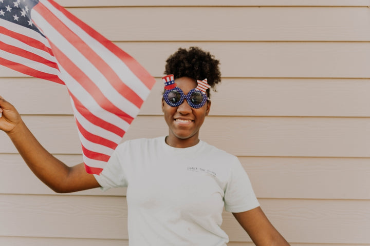 Girl celebrates with an american flag and sunglasses.