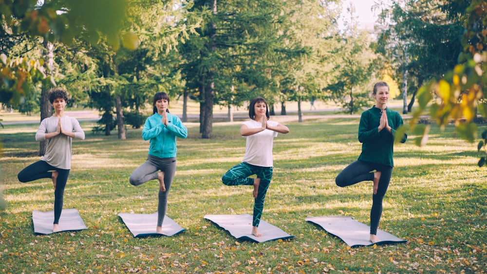 Four women doing yoga tree pose in a park.
